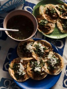 Fotografía de dos plato servidos con tacos de birria con cebolla y cilantro. Además un tazón con consome. 