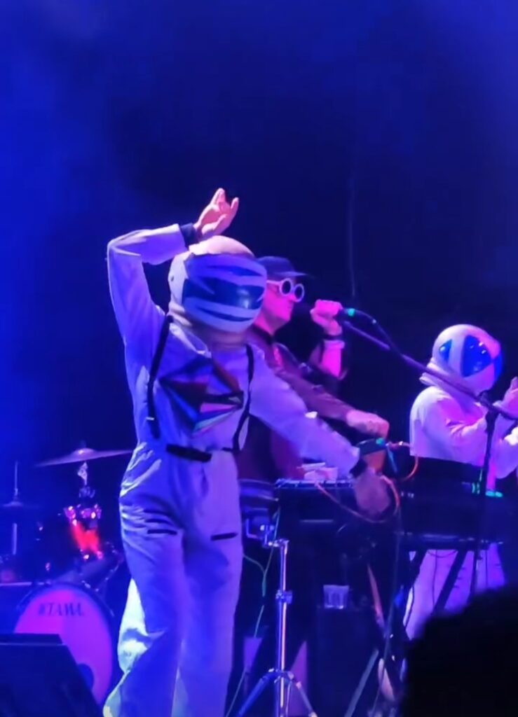 Astronauta con traje con portada del álbum Julius en el escenario con STRFKR